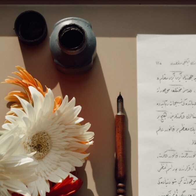 A vintage still life featuring flowers, a calligraphy pen, and handwritten script, capturing artistic romance.