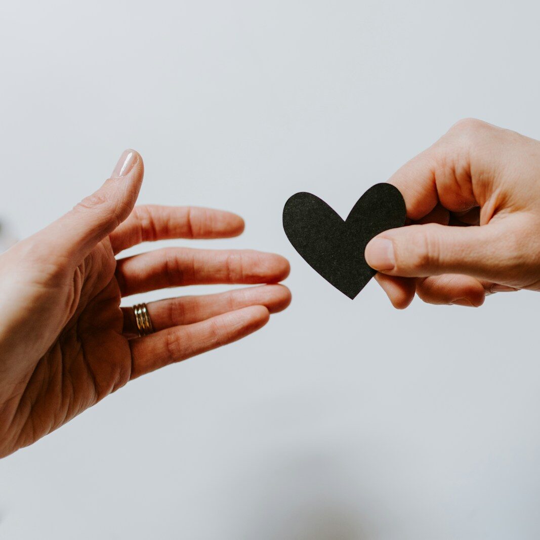 person reaching black heart cutout paper